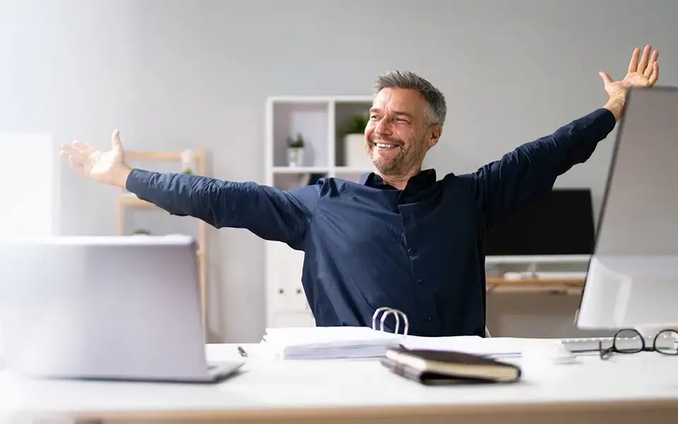 Mann streckt sich glücklich am Schreibtisch